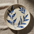 Ivory ceramic plate with hand-painted blue leaves on natural linen