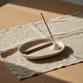 Ivory ceramic incense holder with incense sticks on linen and pale wood